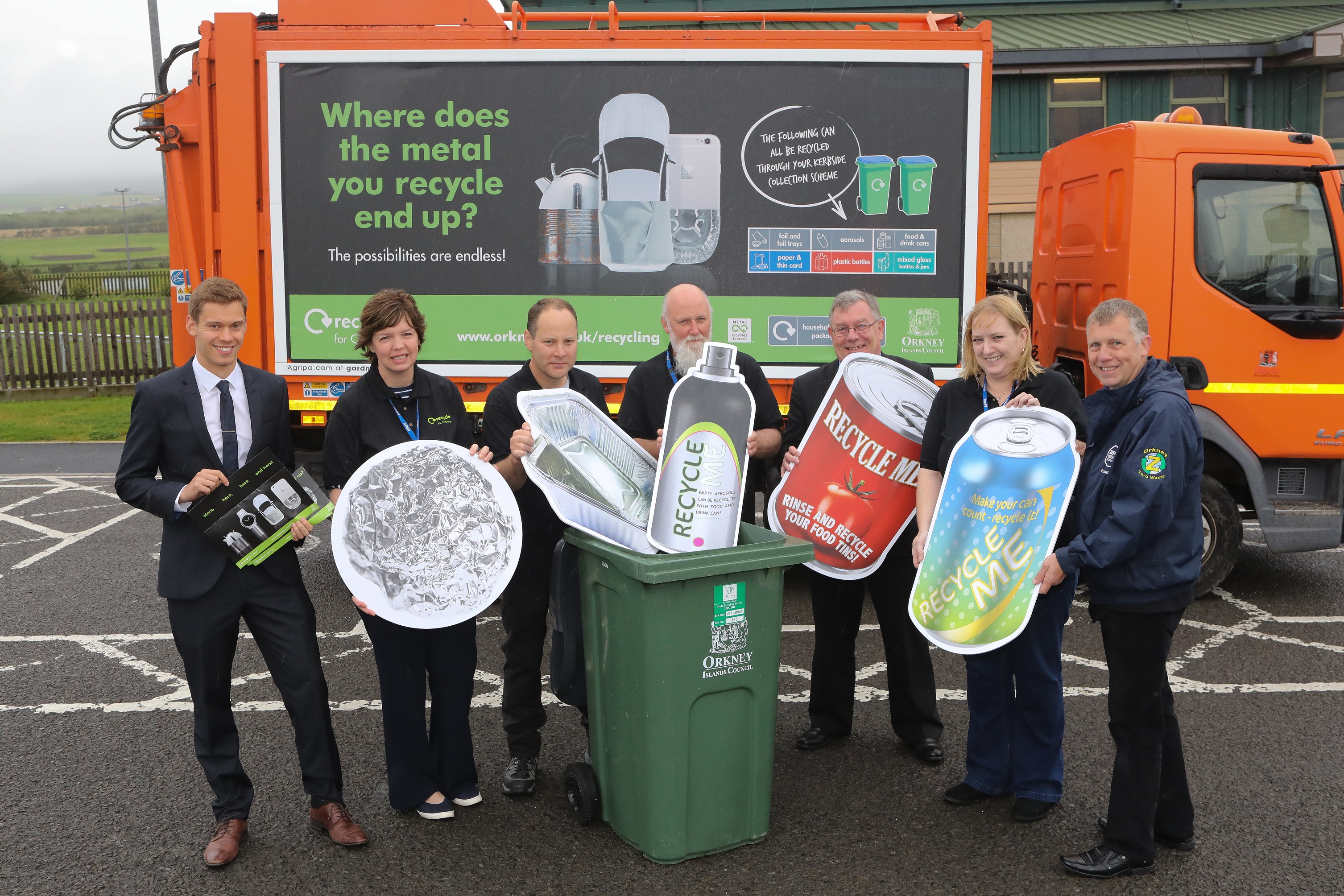 A group of representatives from MetalMatters and Orkney Council holding cardboard cut-outs of metal packaging items in front of one of their recycling vehicles which bears the MetalMatters signage artwork.